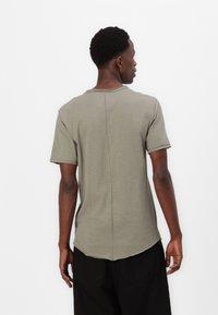 Olivengrünes T-Shirt mit kurzen Ärmeln aus weichem Stoff. Abgerundeter Saum mit sichtbaren Nähten und einer Rückennaht für zusätzlichen Interessant.