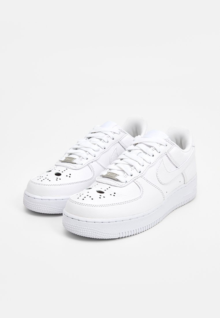 Zapatillas Nike Air Force 1 blancas con puntera perforada, superficie de cuero suave, cordones planos y suela de goma con textura en el dibujo.