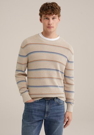 Suéter de punto beige con rayas horizontales azules y naranjas, cuello redondo y puños acanalados. Llevado sobre unos jeans de mezclilla azules.
