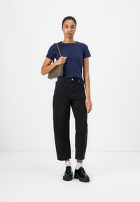 T-shirt bleu marine à manches courtes, jeans noirs taille haute à jambes droites, associés à des chaussures noires imposantes et un sac bandoulière marron.