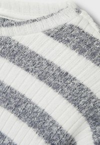 Neulepaita valkoisilla ja harmailla raidoilla, jossa on teksturoitu pinta ja ribbauskaulus, esittelee pehmeää ja lämmintä kangasta.