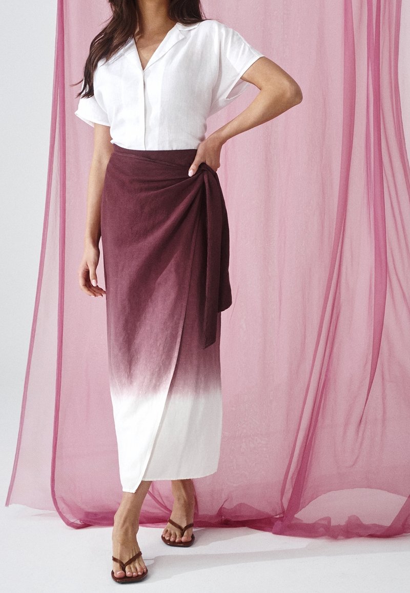 Wit linnen overhemd met korte mouwen gecombineerd met een wikkelrok in bordeauxrood en wit ombré, met een gladde textuur en een eenvoudige silhouet.