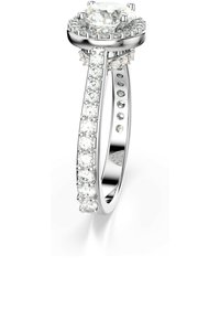 En ring i vitt guld med en stor central diamant, omgiven av mindre diamanter längs med banden, vilande på en slät yta.