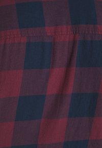 Tessuto a quadri rosso e blu navy con una texture morbida. Presenta quadri di dimensioni uguali, cuciture a punto e una leggera lucentezza.