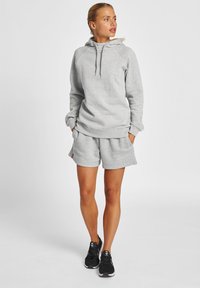 Jasnos szary hoodie z kapturem na sznurku, w zestawie z dopasowanymi szortami. Charakteryzuje się luźnym krojem, ściągaczami przy rękawach oraz bocznymi kieszeniami. Czarne trampki.