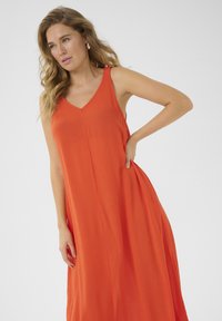 Lång orange klänning med V-ringning och justerbara band, med en flödande design och vertikala sömmar för extra detaljer.