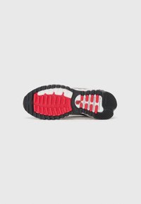 Semelle en caoutchouc noire, rouge et blanche d’une chaussure de sport avec grip texturé et motifs de la semelle conçus pour la traction et la flexibilité.