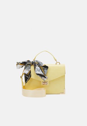 Bolso amarillo de piel sintética de cocodrilo con asa superior, cierre dorado, correa amplia para el hombro desmontable y un pañuelo negro, blanco y dorado con estampado atado al asa.