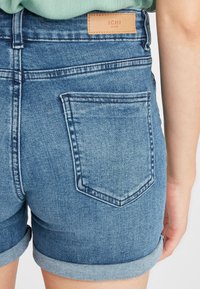 Denim šorti ar sarullētu apakšmalu, gaiši zili. Izceļas ar ādas uzlīmi ar tekstu "ICHI" jostas daļā un vienu aizmugures kabatu.