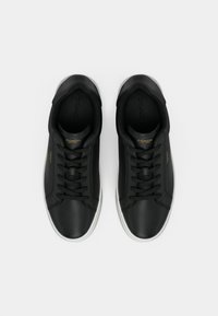 Černé kožené tenisky s kulatou špičkou, plochými tkaničkami a bílou gumovou podrážkou. Zvýrazněné zlatým logem na boku a jazyku.