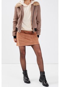 Houndstooth bomberjacka med faux fur-krage, krämfärgad ribbad hoodie, brun mockaskjorta, svarta lackade ankelstövlar med nitar.