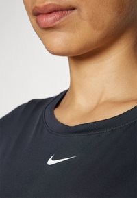Czarna sportowa koszulka z okrągłym dekoltem, z małym białym logo Nike na klatce piersiowej. Gładka faktura, minimalne przeszycia.