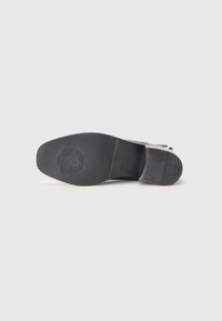 Semelle de chaussure en cuir noir avec une texture lisse, forme de orteil rectangulaire et détail de logo en relief. Design plat pour un maintien stable.