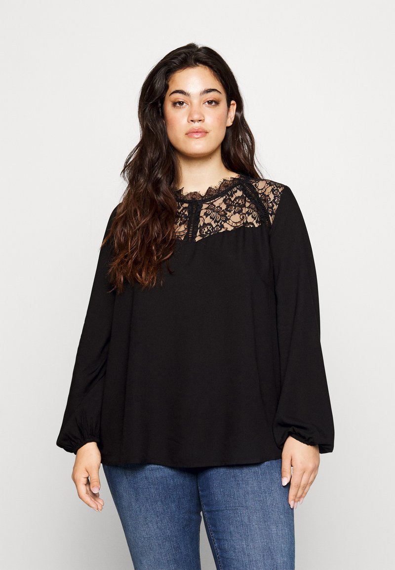 Melna blūze ar garām pūkainām piedurknēm, mežģīņu yoku un apaļu kakla izgriezumu. Mīksta auduma, ar brīvu piegriezumu un smalku mežģīņu akcentiem.