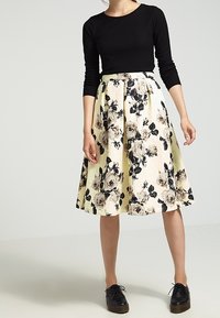 Maglietta nera a maniche lunghe abbinata a una gonna floreale gialla fino al ginocchio con rose nere e beige. La gonna presenta un design plissettato e un tessuto testurizzato.