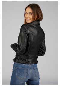 Schwarze Lederjacke mit strukturiertem Kragen und Schnallenverzierungen, ausgestattet mit einem taillierten Schnitt und sichtbaren Nähten über glattem Material.