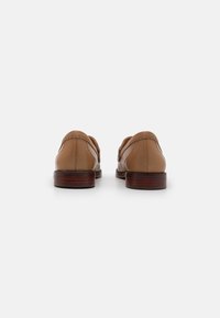 Brown leather slip-on shoes with a smooth finish, featuring decorative stitching and a low wooden heel. Back view showcases clean lines.