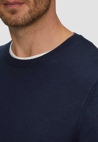 Marineblauwe trui met een ronde hals. Gemaakt van zachte stof, met een geribbelde kraag en een gladde textuur, zichtbaar stikseldetail.