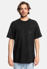 Černé tričko s krátkým ruk ávem vyrobené z bavlny, s náprsní kapsou a čtvercovou logem nášivkou. Rovný střih a kulatý výstřih, minimalistický design.