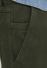 Green cotton cargo pants with a smooth texture, featuring a front pocket and visible stitching details.