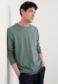 Olivgrön långärmad T-shirt i mjukt tyg, med rund halsringning och bröstficka. Styla med mörka byxor.