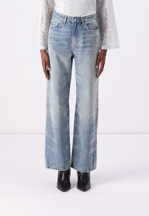 Lichtblauwe wijduitlopende jeans met een vervaagde afwerking en subtiele slijtage details, gecombineerd met zwarte enkelboots en een sprankelend zilveren top.