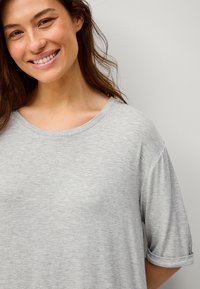 Světle šedé tričko s krátkými, ohrnutými rukávy, vyrobené z měkké látky, s tradičním kulatým výstřihem a volnějším střihem.
