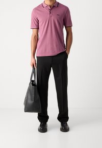 Rosa bomullspolo med svarta detaljer, kombinerad med svarta byxor och bärande på en svart läderhandväska. Svarta skor fulländar looken.