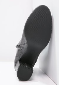 Zapato de tacón alto negro con parte superior de cuero texturizado similar a piel de reptil y suela de goma lisa. Cuenta con un tacón moderado y una hebilla decorativa.