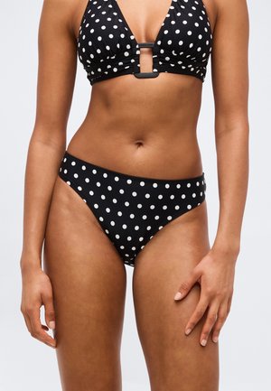 Bikini noir à pois blancs, comprenant un haut à col plongeant avec une découpe centrale et un bas taille basse assorti porté par un modèle mince.