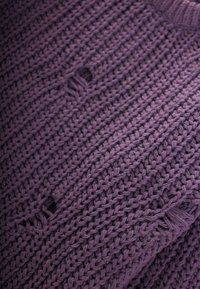 Maglione lavorato a maglia in viola scuro, caratterizzato da un motivo testurizzato con punti larghi e un piccolo foro, che evidenzia un design rilassato.