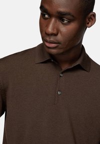 Polo de punto marrón con cuello, que presenta una tapeta de tres botones, una sutil textura de canalé y un diseño ligeramente ajustado.