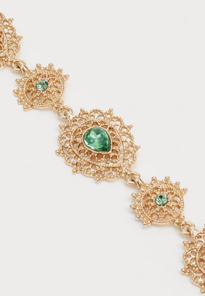 Pulsera de encaje dorado con un intrincado diseño de filigrana, adornada con tres piedras esmeralda verdes facetadas en forma de lágrima y redonda.