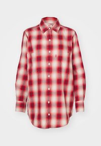 Chemise à manches longues à carreaux rouges et blancs, boutonnée avec col et deux poches poitrine, présentée sur un fond blanc.