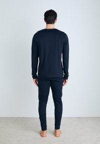 Marineblauwe langemouw top met ronde halslijn, gecombineerd met marineblauwe broek met een subtiel stippenpatroon, gemaakt van zachte, gladde stof.