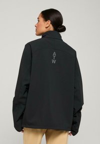 Černá softshellová bunda s vysokým límcem, volným střihem a oversized rukávy. Na zadní části se nachází logo "ATW" v šedé barvě. Jednoduchý design, hladká textura.