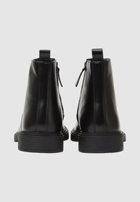 Stivali ankle in pelle nera con finitura liscia, dotati di cerniere posteriori e una suola spessa e texturizzata. Design semplice con linguette per la calzata.