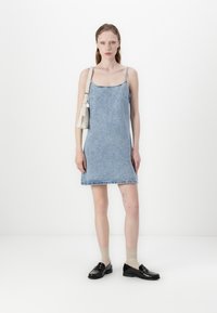 Traper haljina s tankim trakama, svijetloplave boje, s neobrašenim rubom, uparena s crnim mokasinkama i krem čarapama, dopunjena malom bijelom torbicom.