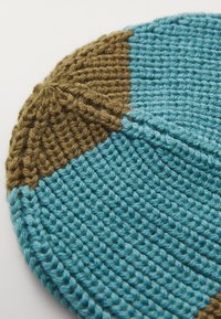 Knitted beanie in blue and brown, featuring a textured pattern with alternating colors and ribbed detailing. Circular shape.