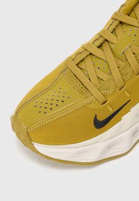 Sapatilha atlética amarela com um upper de tecido texturizado, biqueira reforçada e logotipo preto. Apresenta um design de atacadores e detalhes perfurados para ventilação.