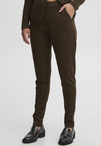 Brown herringbone patterned trousers with a tailored fit, featuring a smooth texture and side pockets, paired with black loafers.