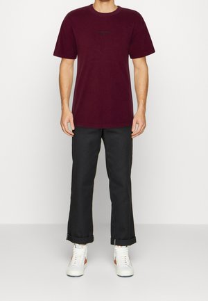 Mørkerød bomulds-t-shirt med rund hals og korte ærmer, kombineret med sorte op rullede bukser og hvide sneakers. Simpelt design uden mønstre.