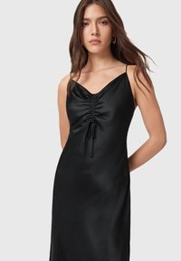 Abito in raso nero con scollatura a V, spalline sottili e dettagli arricciati sul seno con legature regolabili. Tessuto morbido e silhouette aderente.