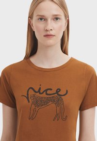 Brun bomulds T-shirt med et sort leopard grafik og ordet "nice" skrevet i en flydende skrift. Kortærmet og rund halsudskæring.
