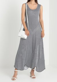 Czarna i biała sukienka maxi w paski z dekoltem w serek, ozdobiona geometrycznymi wzorami, luźnym krojem i rozcięciami po bokach; zestawiona z białą torebką i sandałami.