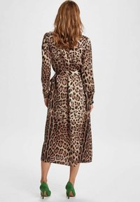 Midi šaty s leopardím vzorom vyrobené z hodvábneho materiálu, s dlhými rukávmi, úzkym pásom a voľnou sukňou. Skombinované s zelenými lodičkami.