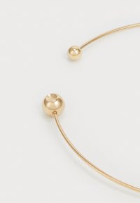 Pulsera de metal en tono dorado con dos acentos esféricos y un diseño de alambre curvado. Textura suave con acabado pulido.