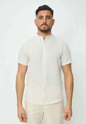 Chemise à manches courtes, col classique, de couleur crème clair avec de subtiles rayures bleues, dotée d'une fermeture bouton et d'un tissu texturé.