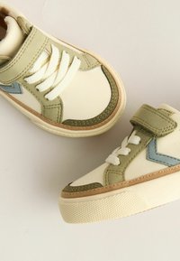 Lysecreme sneakers med grønne og blå accenter, tekstureret creme sål, bomulds snørebånd og Velcro-rem; ruskinddetaljer på siderne.