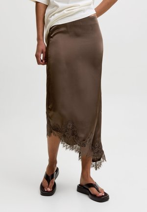 Jupe midi en satin marron avec bordure en dentelle à l'ourlet, portée avec un top blanc et des sandales à plateforme noires sur un fond clair.